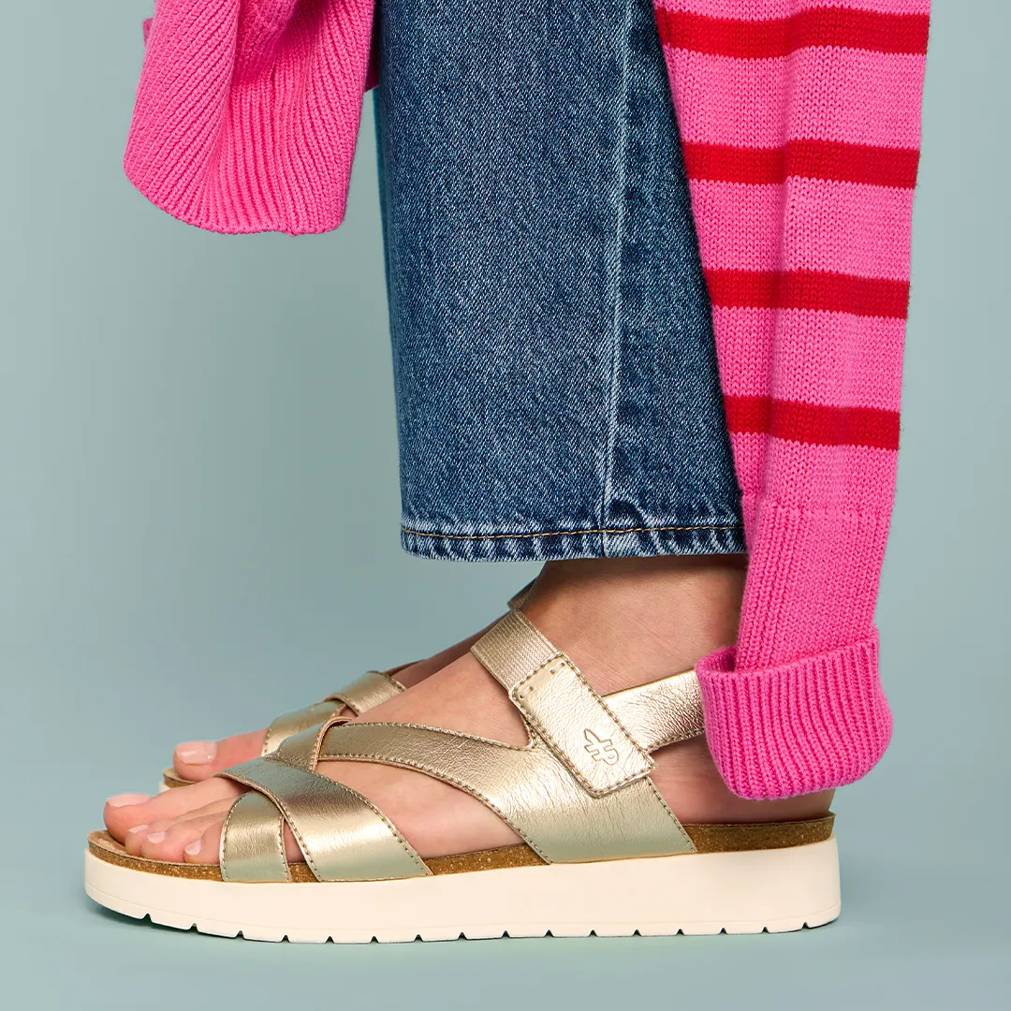 A woman in pink-and-red striped sweater, blue jeans and the Savoy sandal in metallic Champagne